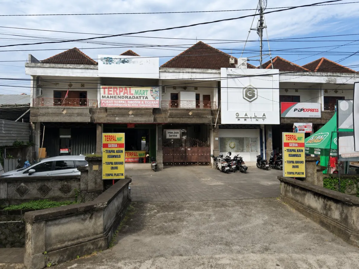 Lokasi Iman Jaya Service di Jl. Mahendradatta — papan kecil di tengah, antara Terpal Mart dan Gala Print, akses lewat pagar coklat